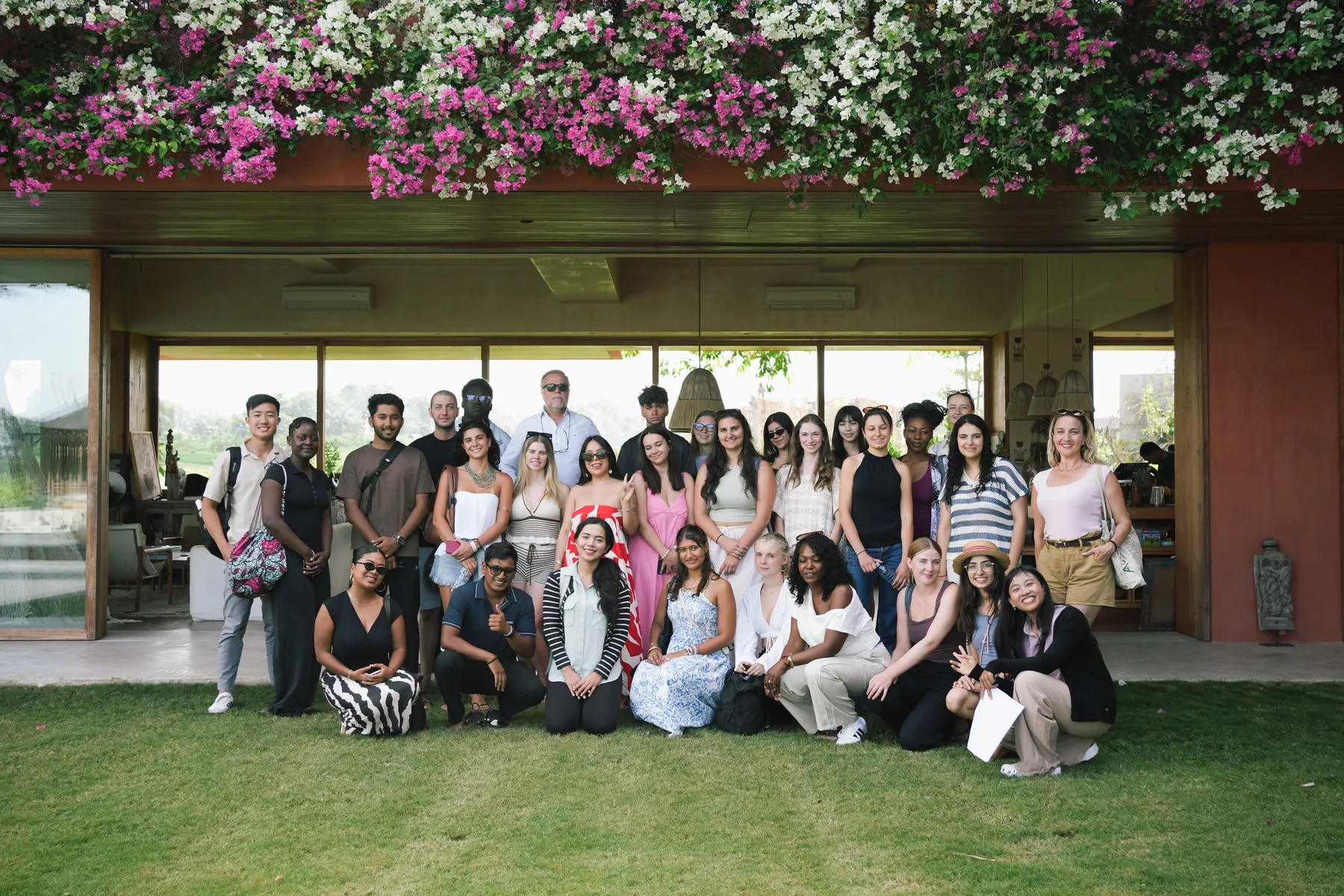 The full Summer School 2026 group on the lawn at Nenek Coco Villa, under a wall of pink and white bougainvillea