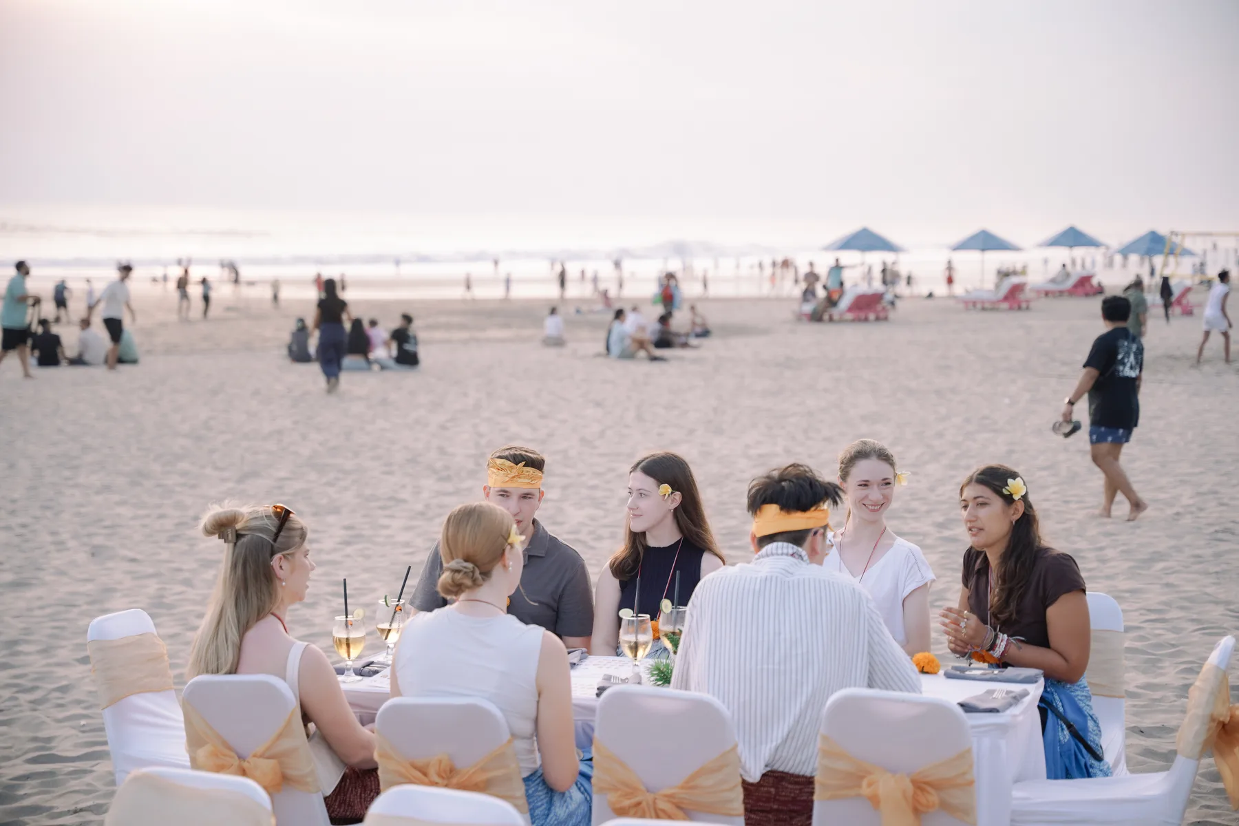 Students seated at a long table on the beach at sunset during the Welcoming Dinner, the sea behind them