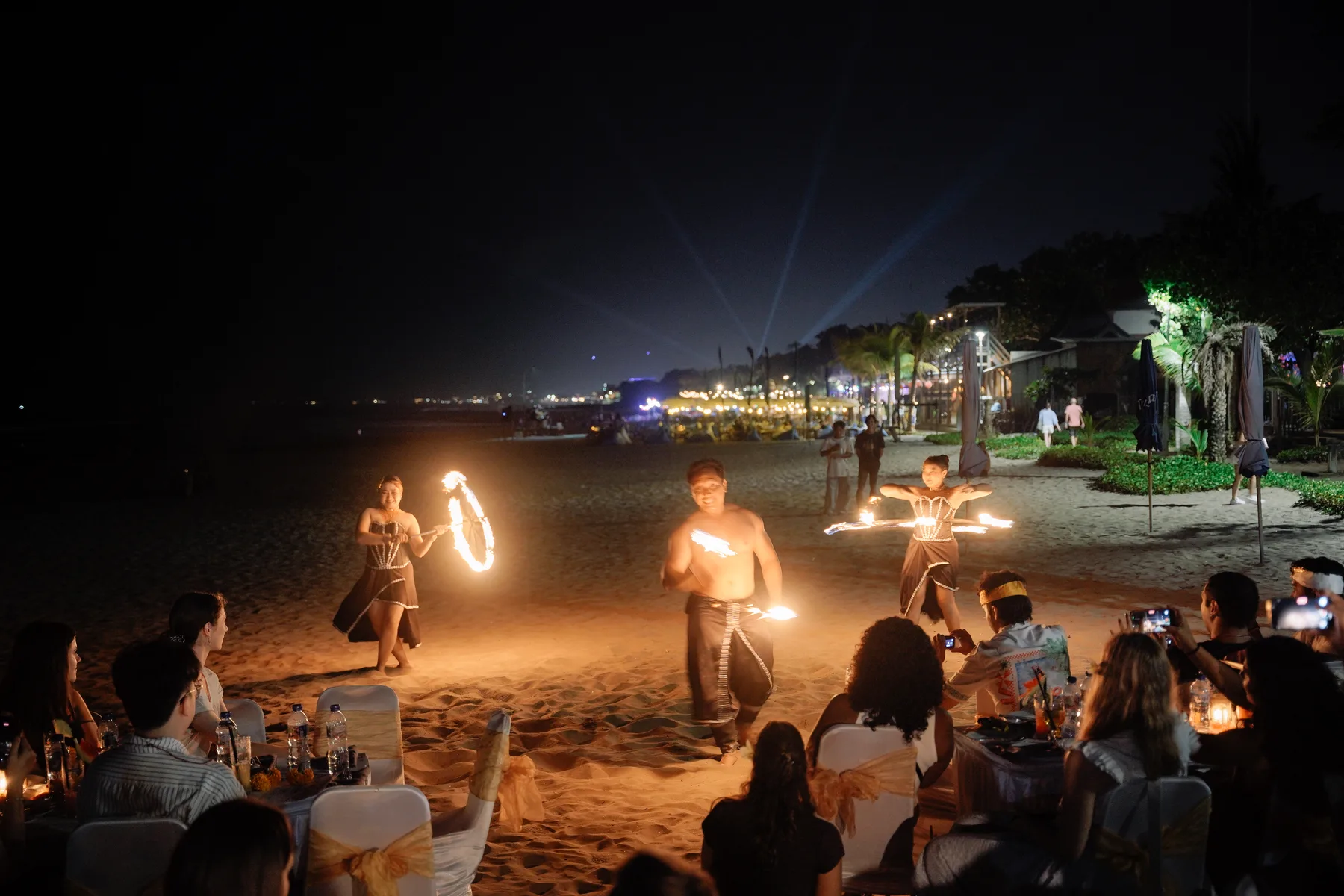 Fire dancers performing on the beach at night in front of the seated Welcoming Dinner guests