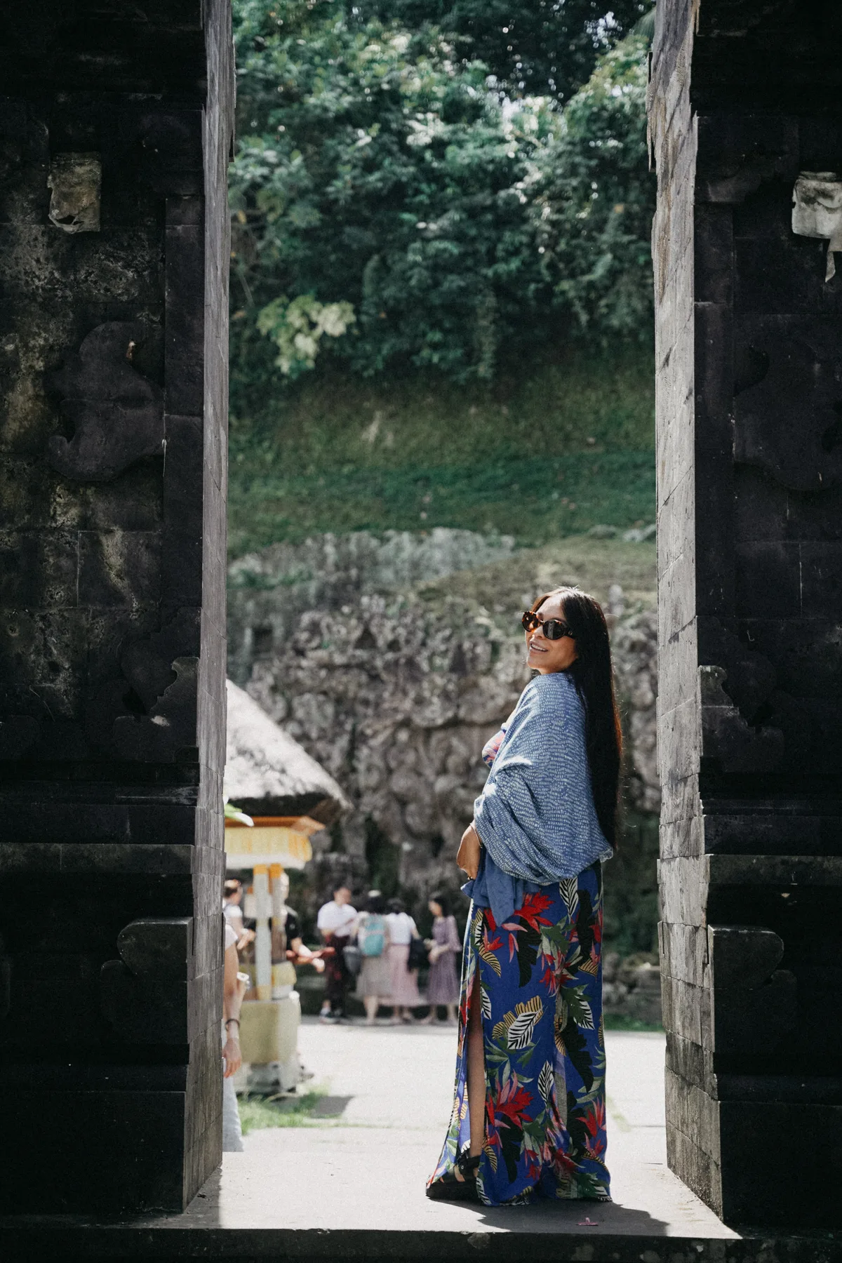 A student standing in the dark stone opening of a split temple gate at Goa Gajah, the courtyard visible beyond