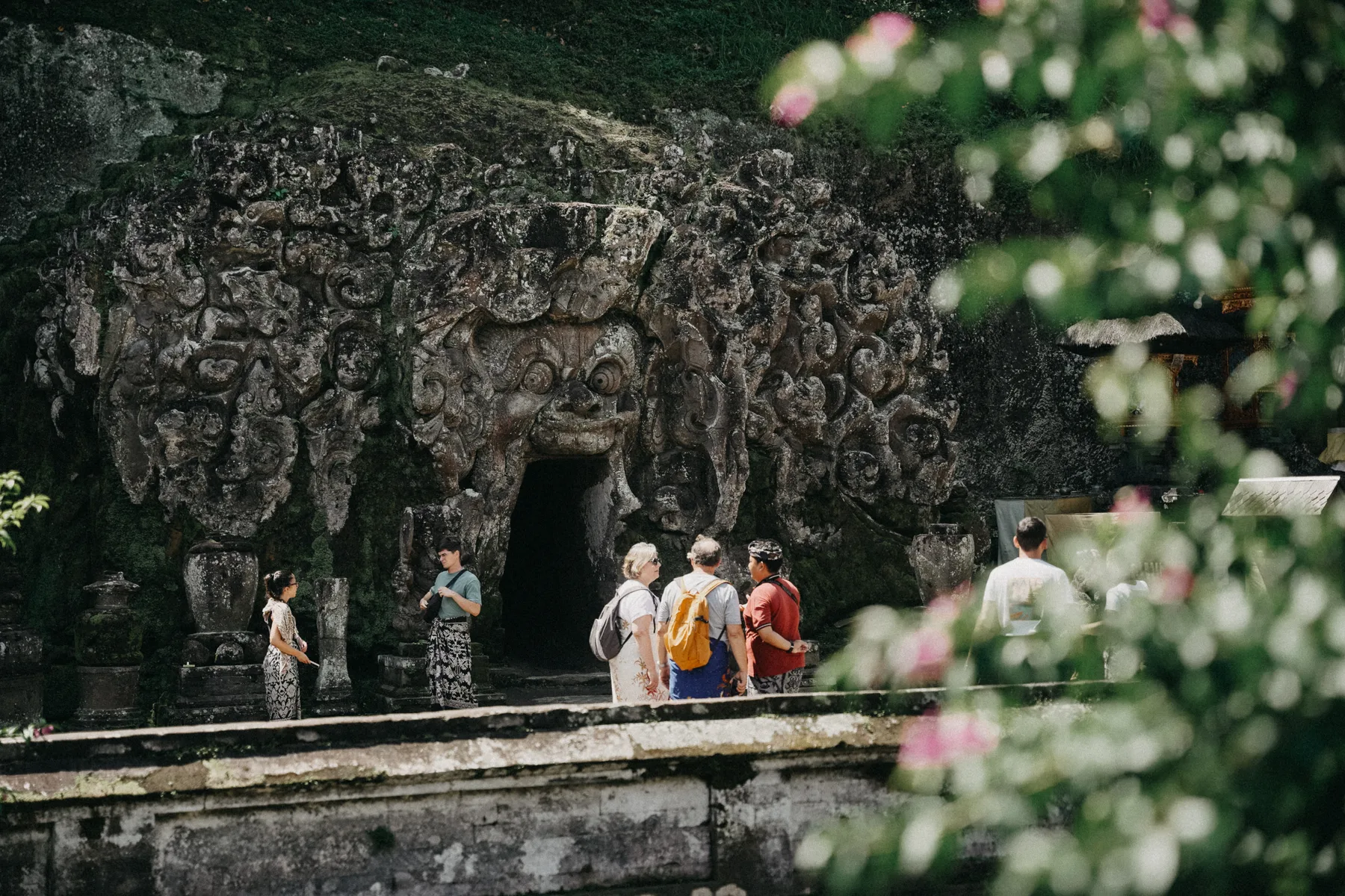 The carved stone facade and entrance of the Goa Gajah elephant cave, with visitors standing before it