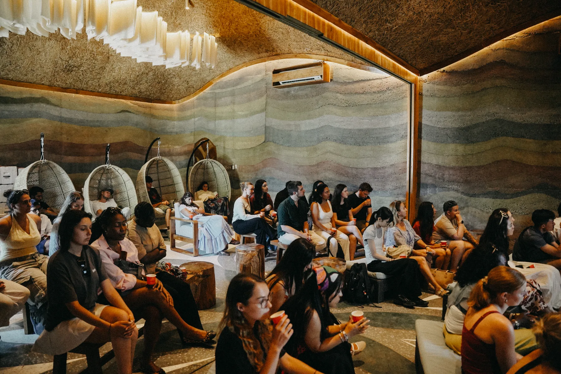 Students seated in a rammed-earth amphitheater lounge with hanging pod chairs at Nuanu