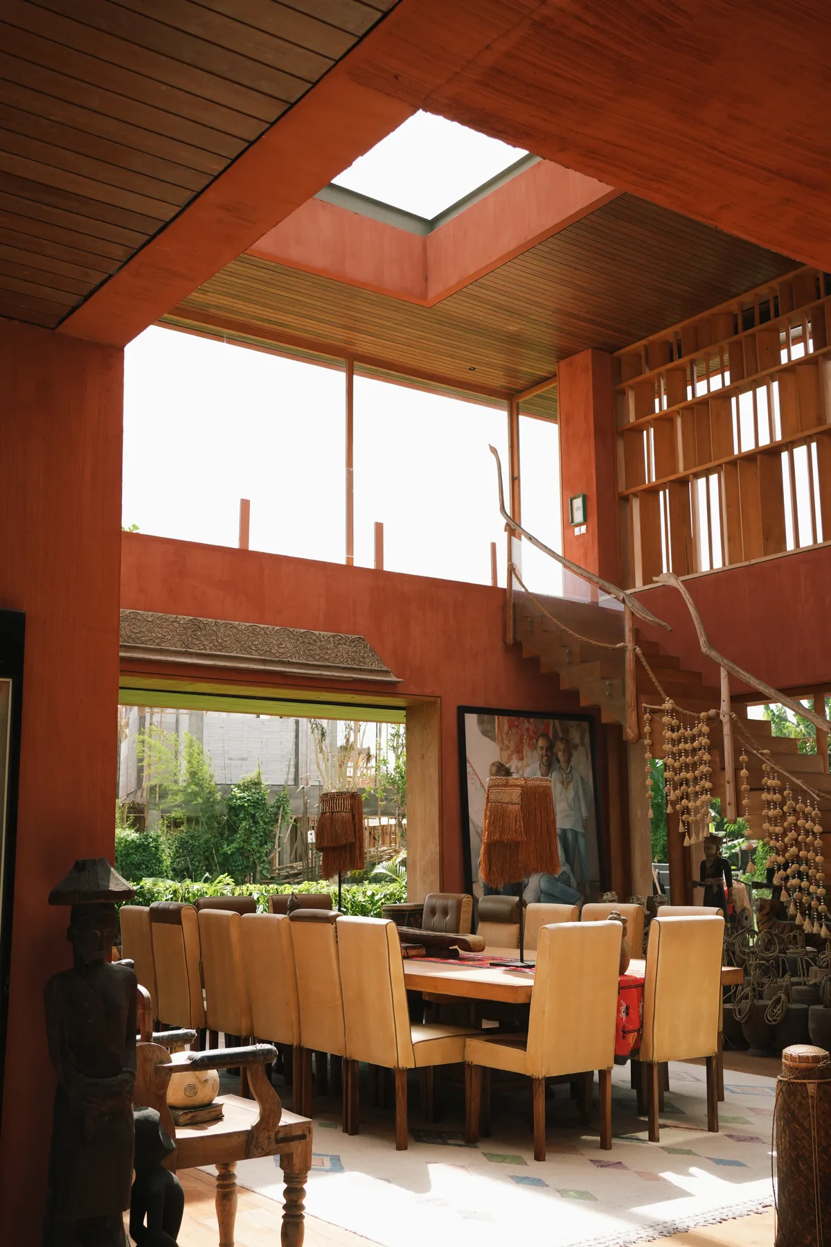 A double-height dining room with a square skylight and a long wooden table at Nenek Coco Villa