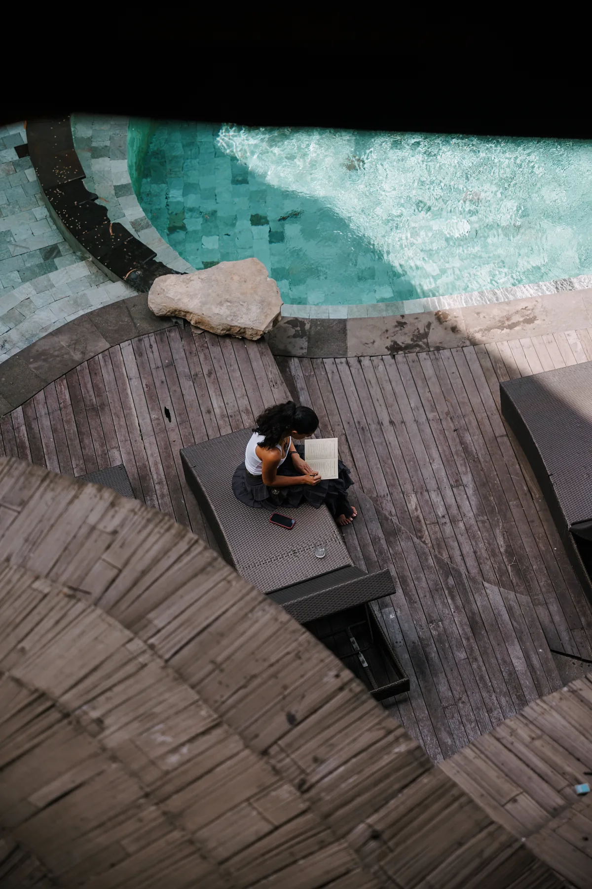 An aerial view over a curved wooden pool deck at BambooU, two people sitting together reading