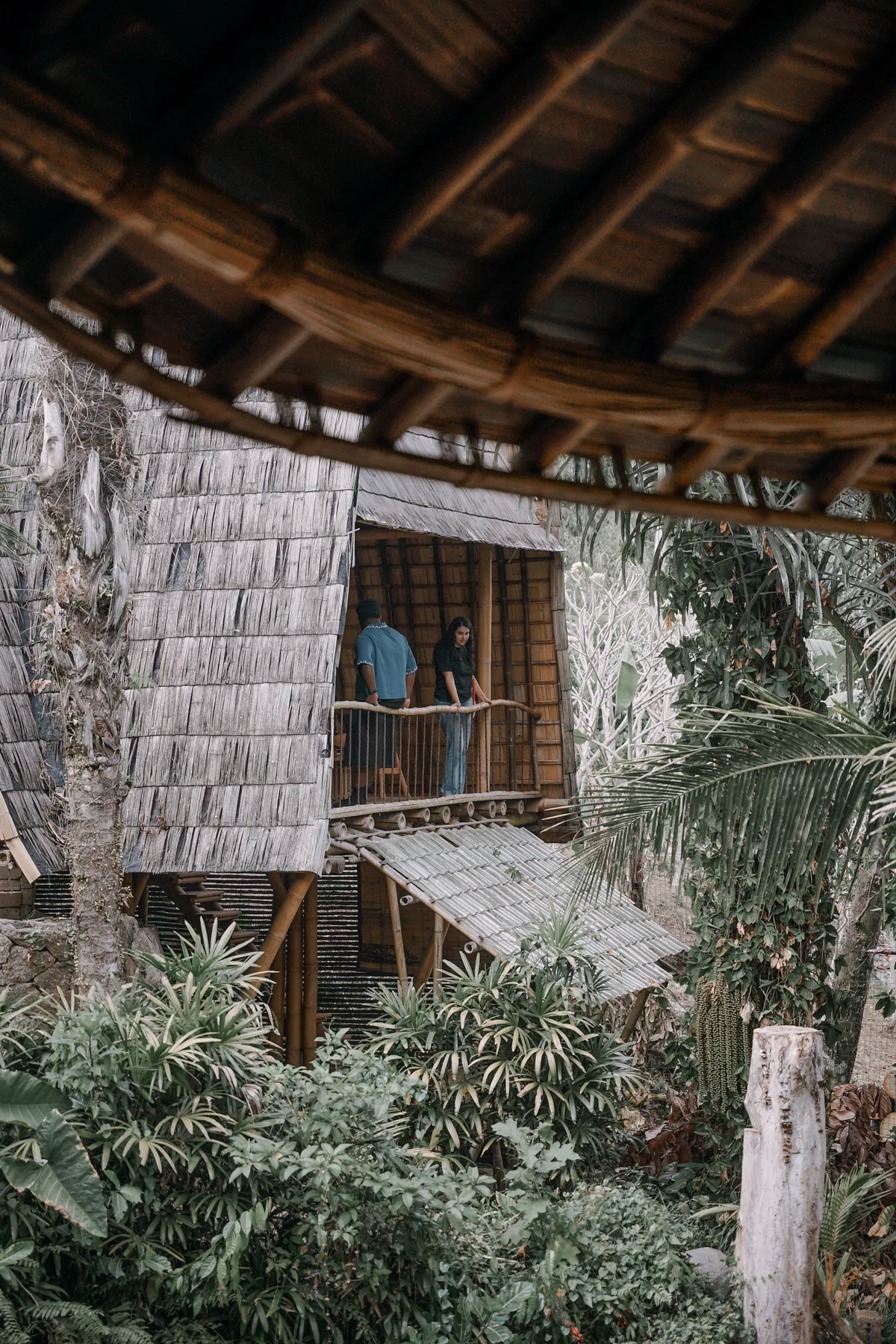 A multi-storey bamboo house at Green Village, its shingled roofs rising out of the jungle, people on the open balcony