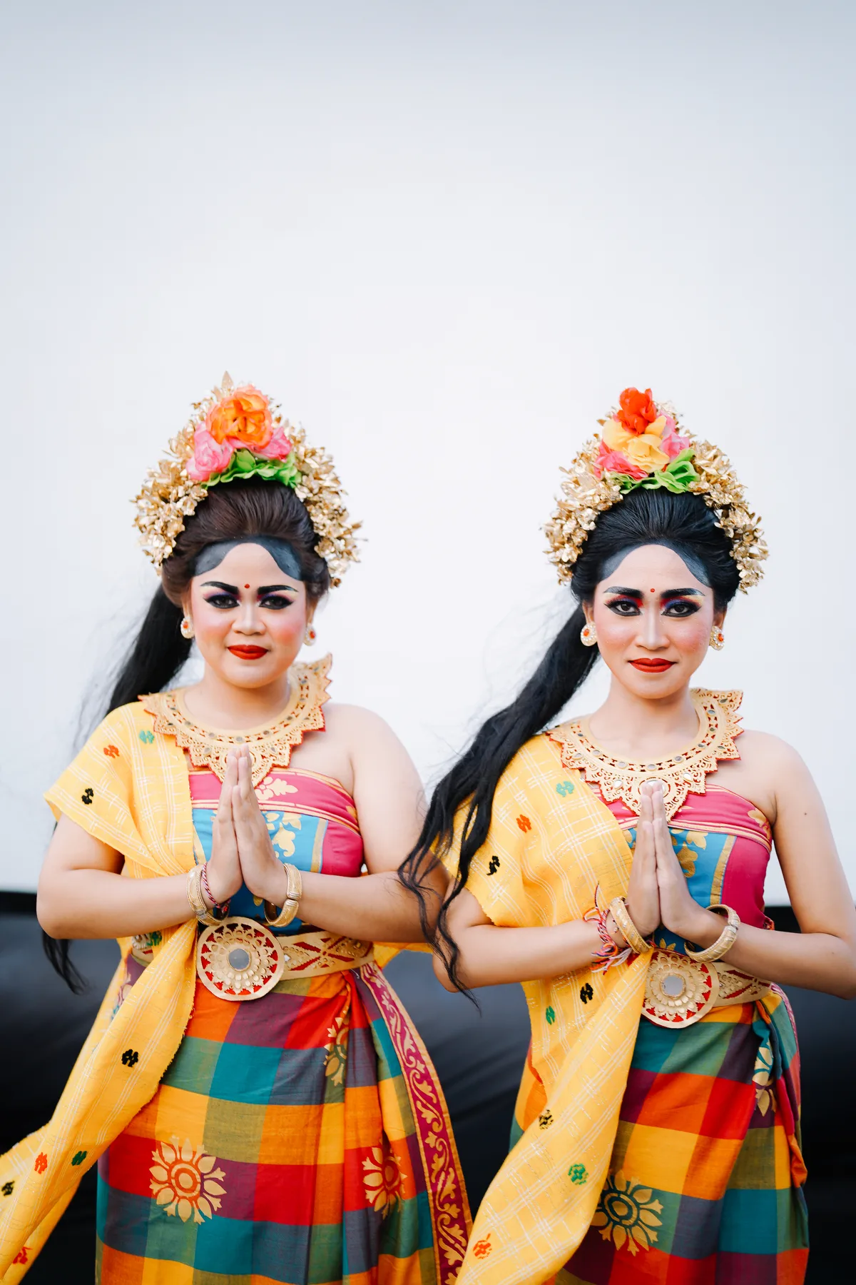Two Balinese dancers in traditional costume and gold headdresses posing with hands together