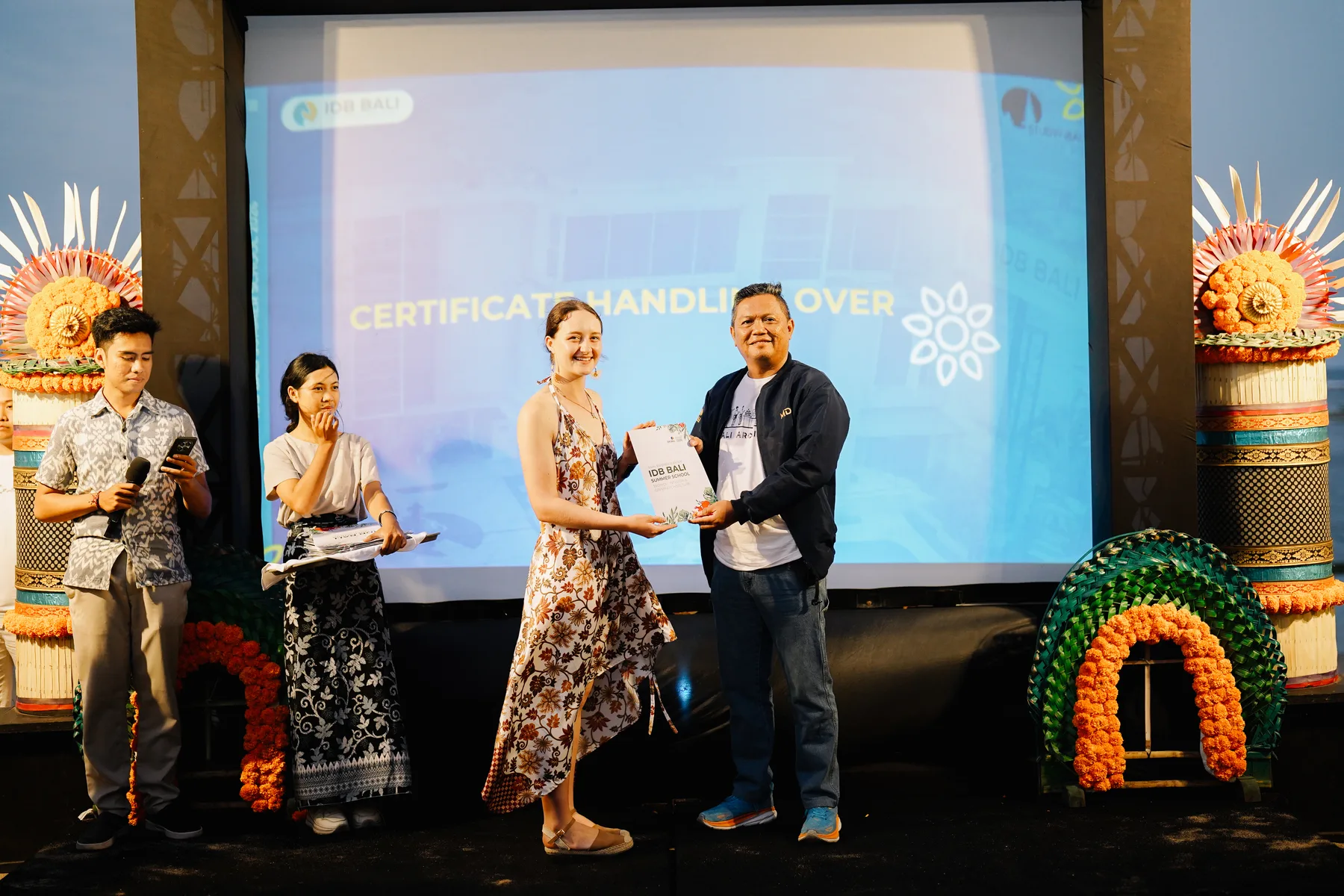 A student receiving her certificate from an IDB Bali staff member on stage during the Certificate Handling Over ceremony