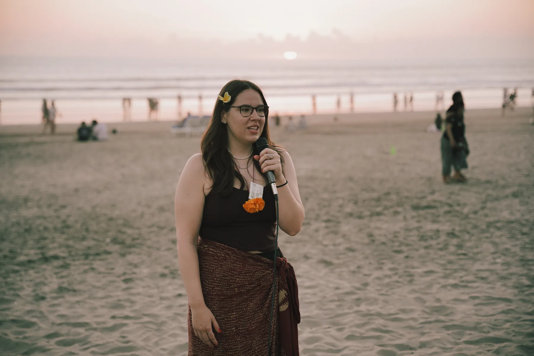 A student speaking into a microphone on the beach at sunset