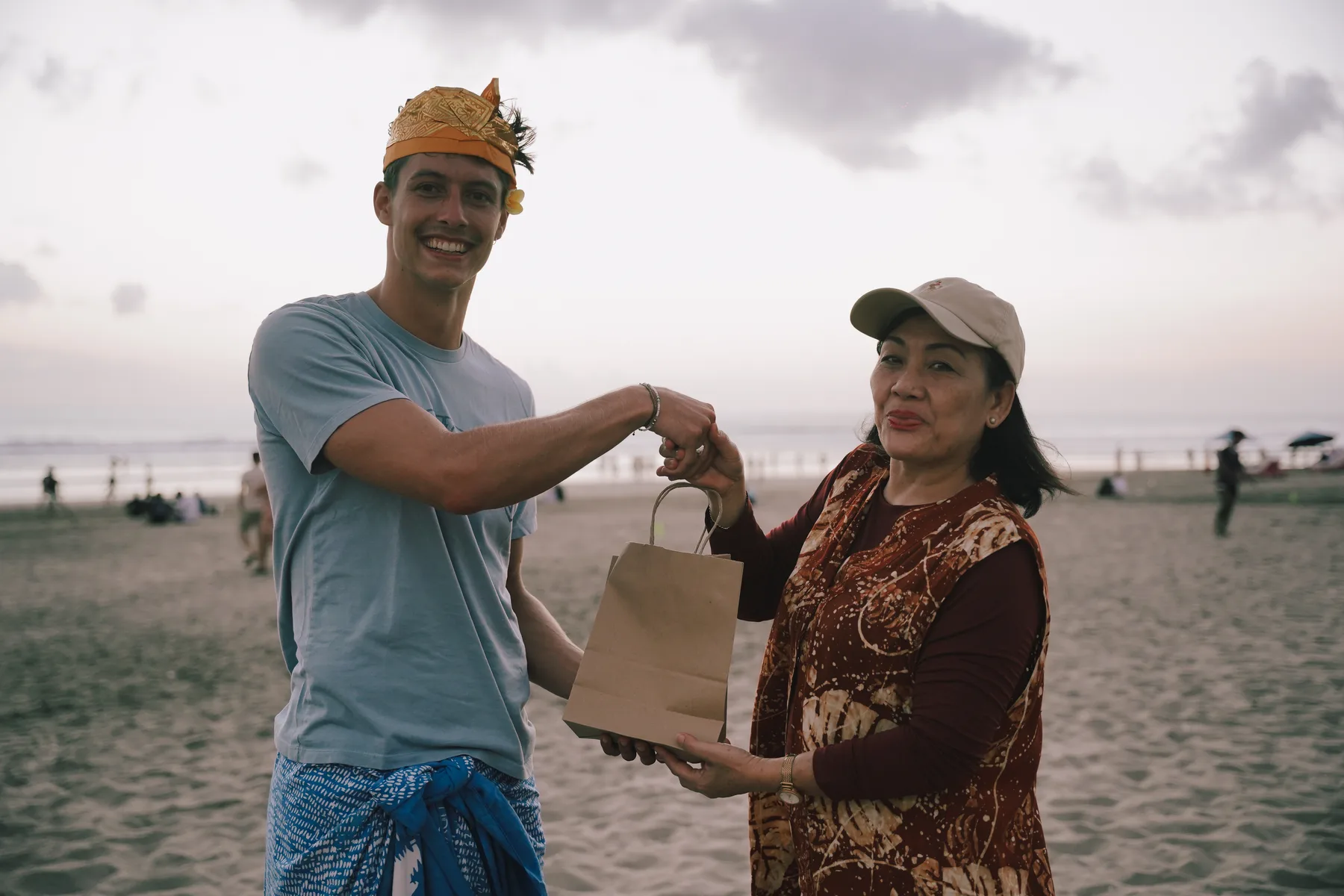 A staff member handing a gift bag to a student in udeng and sarong